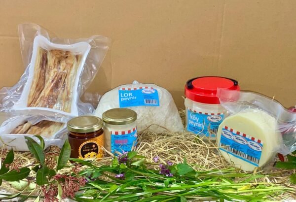 Assorted dairy and bakery items—bread, cheese blocks, jars of honey and jam—displayed on straw with fresh wildflowers in front for a rustic market setup